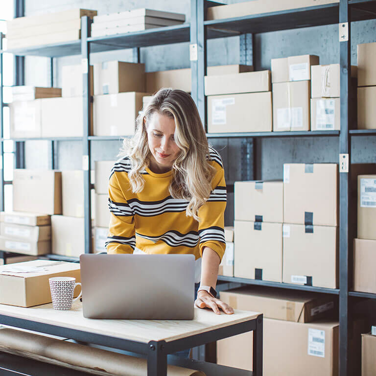 Small business owner on her laptop with shipping boxes behind